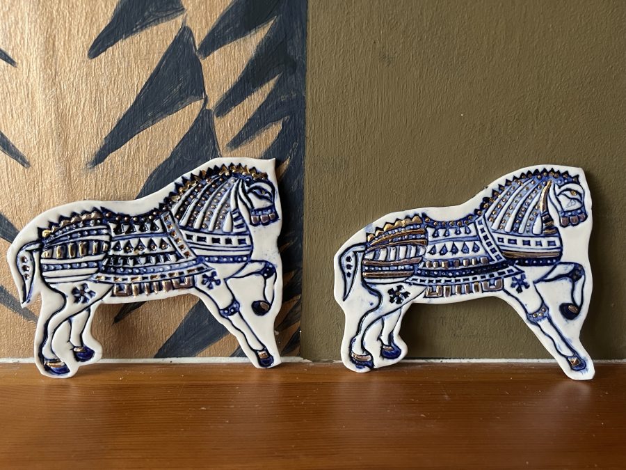 Two blue white and gold patterned porcelain horses displayed on a mantle piece. 
