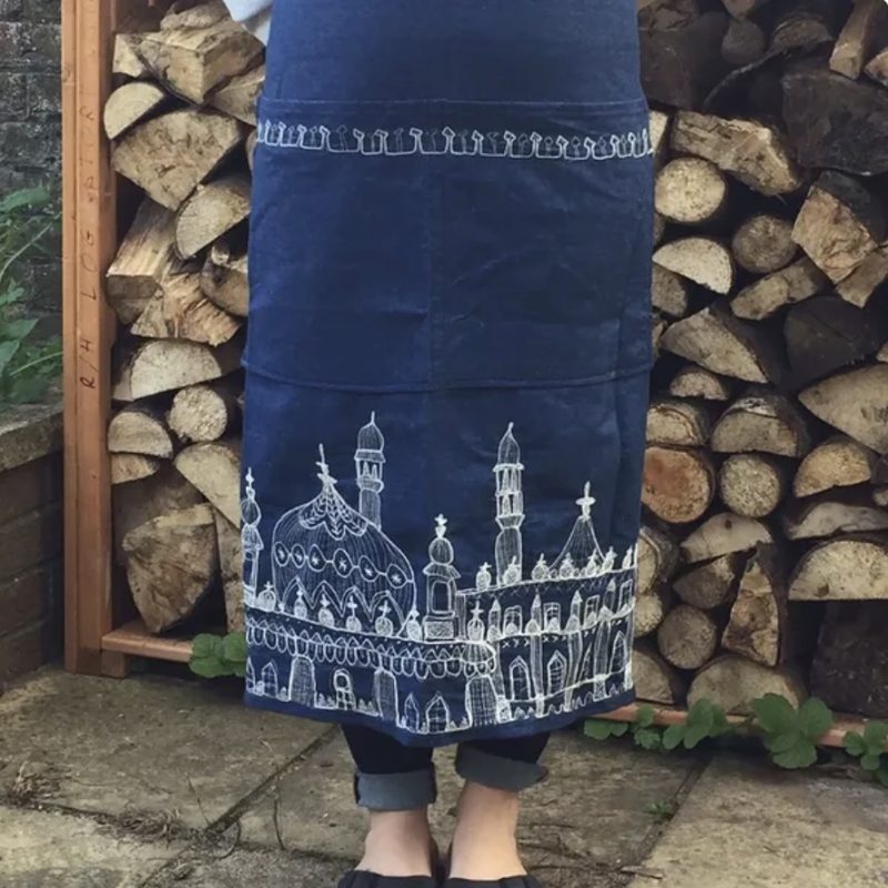 Image of lady wearing a denim pinny with white embroidered image of Brighton Pavillion