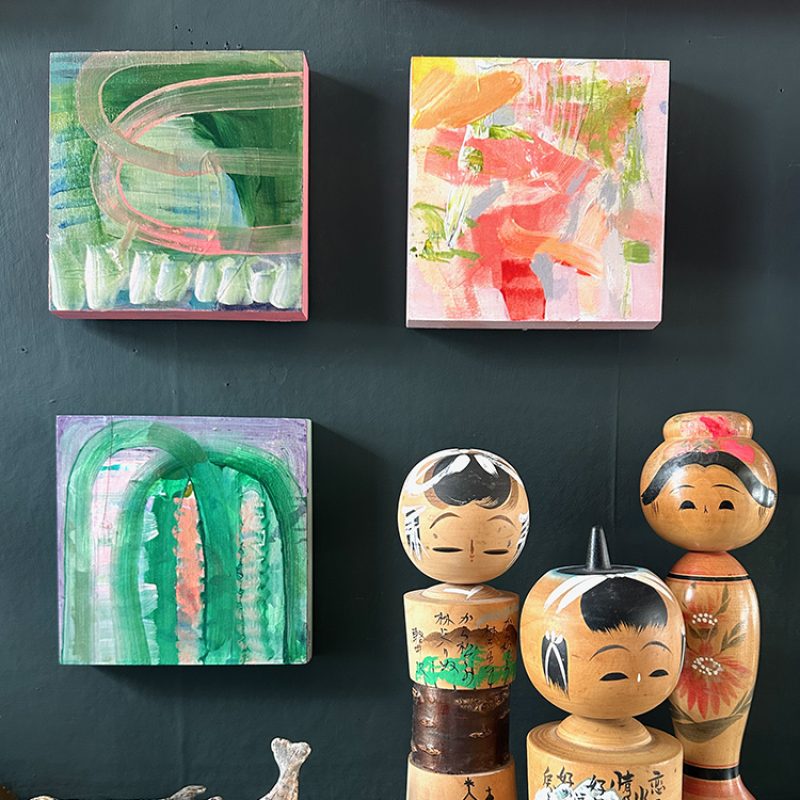 Carved vintage Japanese dolls on shelf with small abstract paintings behind