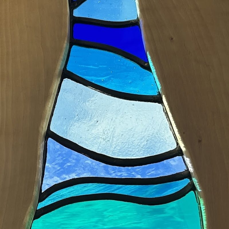 A tall narrow panel of stained glass set in a wooden surface.the glass is set in curved horizontal bands that flow from top to bottom , like ripples or waves.