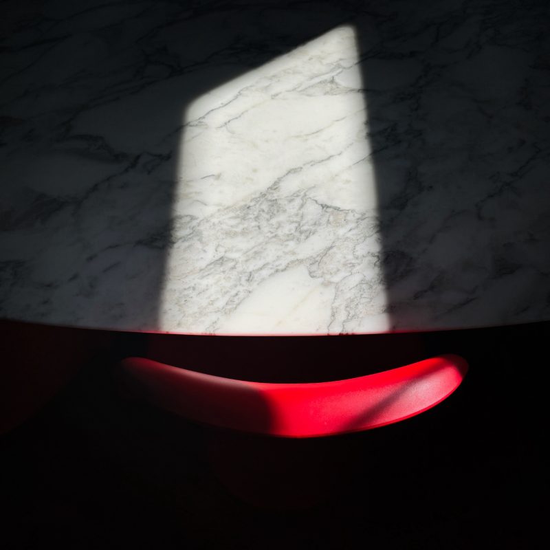 An abstraction of a white marble Eero Saarinen table and a red Verner Panton chair with fragments of sun and shade.