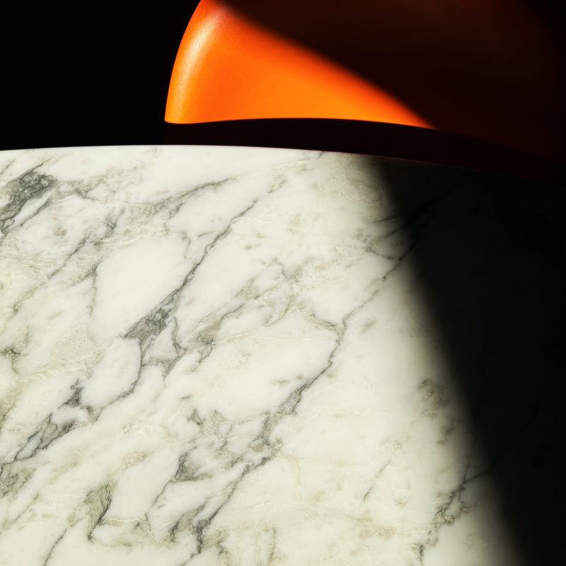 An abstraction of a white marble Eero Saarinen table and an orange Verner Panton chair with fragments of sun and shade.
