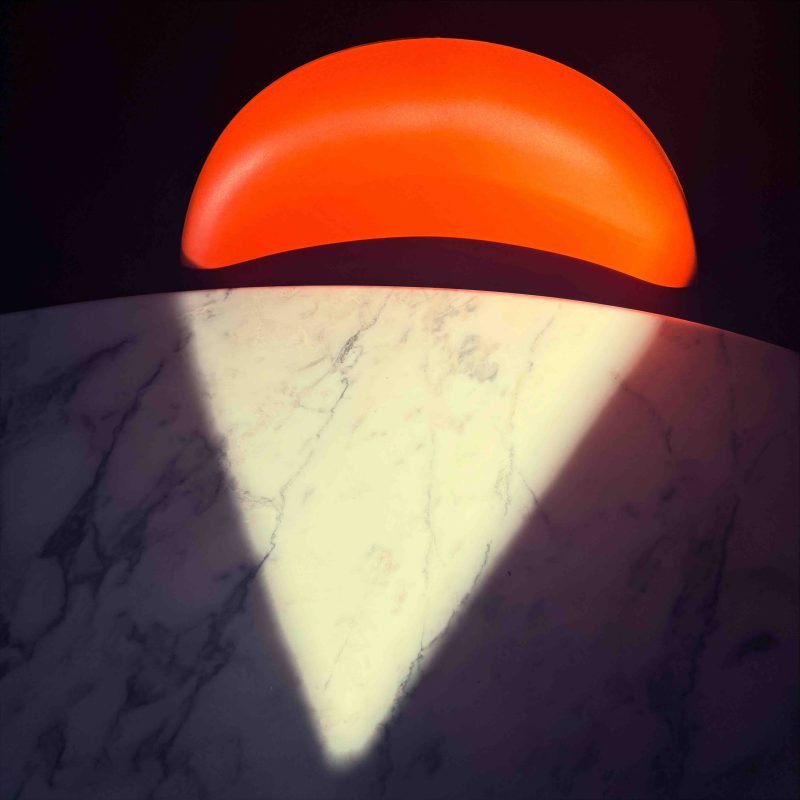 An abstraction of a white marble Eero Saarinen table and an orange Verner Panton chair with fragments of sun and shade.