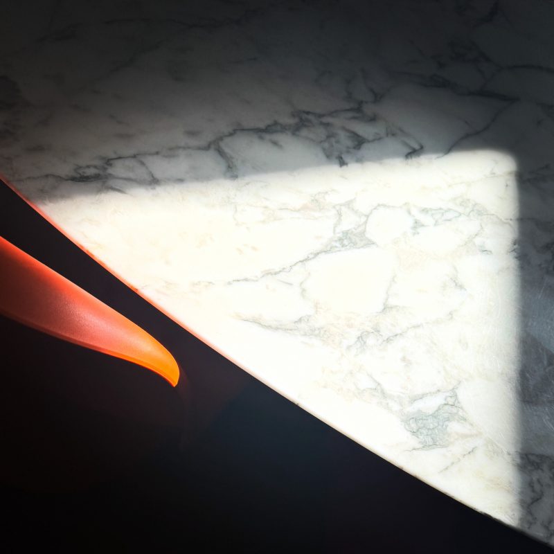 An abstraction of a white marble Eero Saarinen table and an orange Verner Panton chair with fragments of sun and shade.