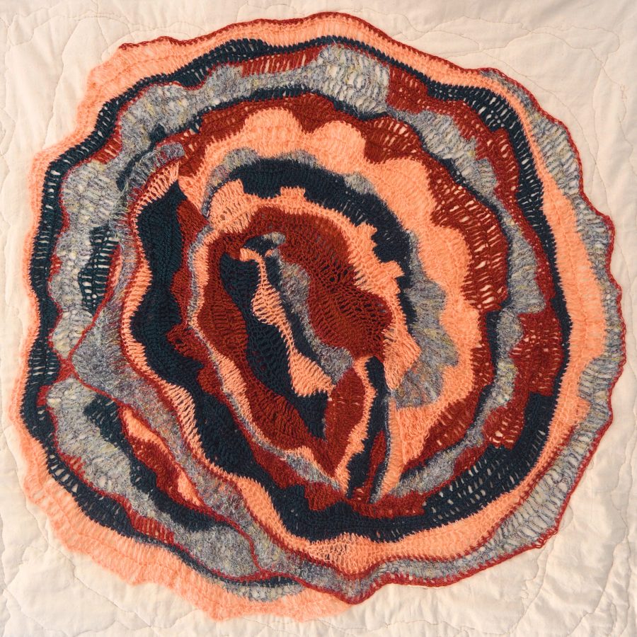 Crochet textile artwork; blue, orange, red, & grey freeform crochet stitches on a quilted canvas backing. 