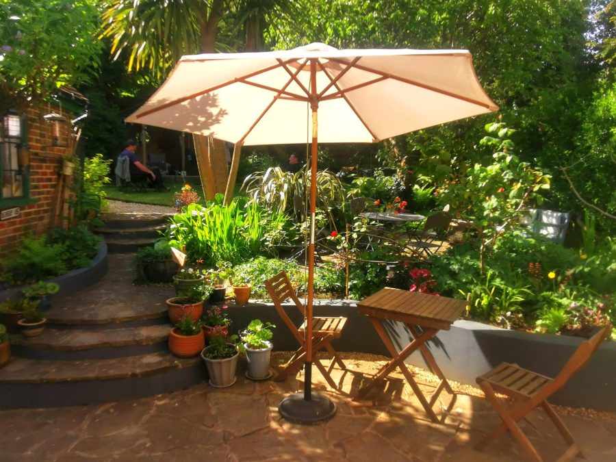 A parasol is in bright sunlight  in a beautiful cottage garden.