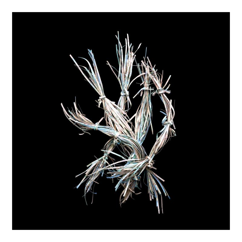 Long strips of a map of Tanzania tied into bundles using shorter strips of the map.  Photographed against a black background.