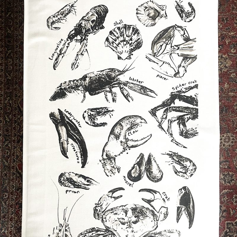 White tea towel decorated with a collection of black sea creature illustrations (lobsters, crabs, langoustine etc.)