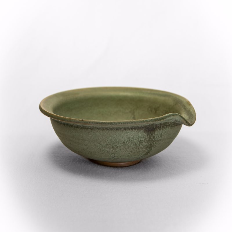 A handmade ceramic pouring bowl with a small pouring lip, glazed in a deep earthy green.