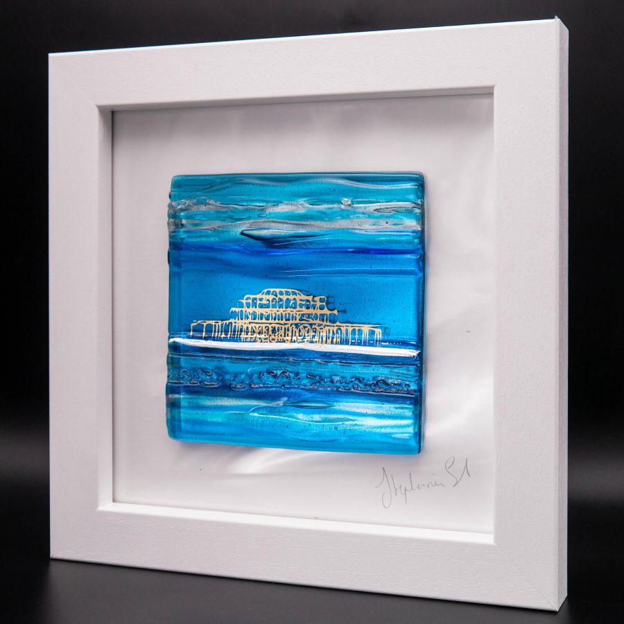 A textured glass tile in shades of aqua and turquoise with an abstract image of Brighton West Pier in shiny 22ct gold