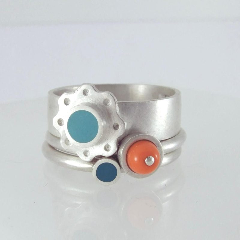 A silver resin inlay ring set compromising of 3 silver stacking rings with a turquoise flower design resin inlay and an orange bead glass inlay