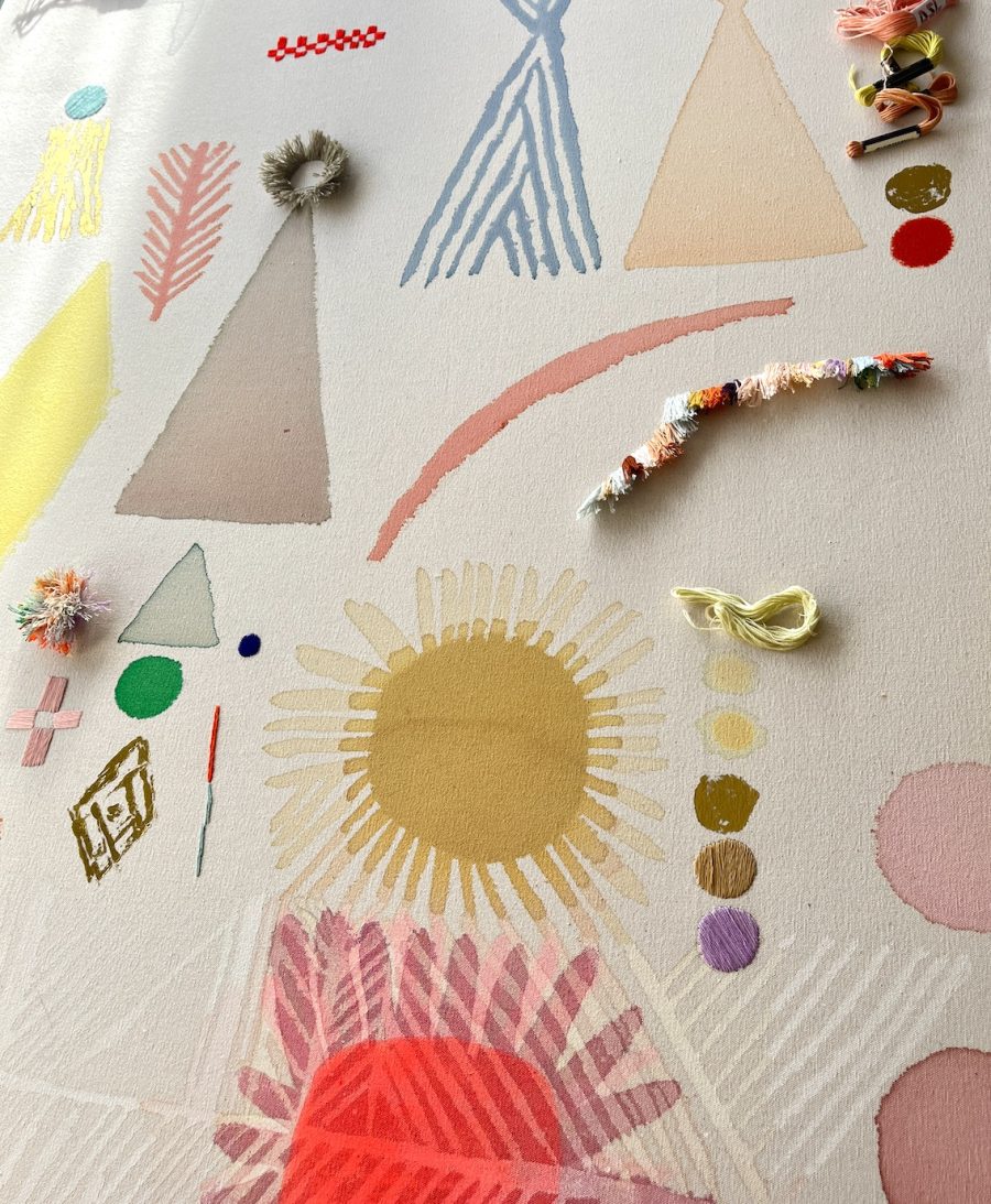 A mixed media painting using bright and pastel colours on raw canvas. Suns, triangles and stripes sit across the surface like a map of ancient symbols. There are gold embellishments in circles and stripes as well as embroidered and tufted areas.