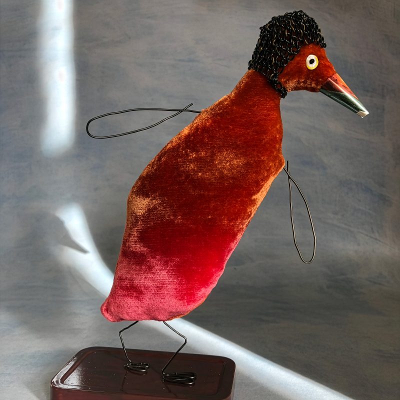 Sculptural bird-like figure. Brown and red velvet body, with wire wings and legs. Knitted wire balaclava. On metal plinth