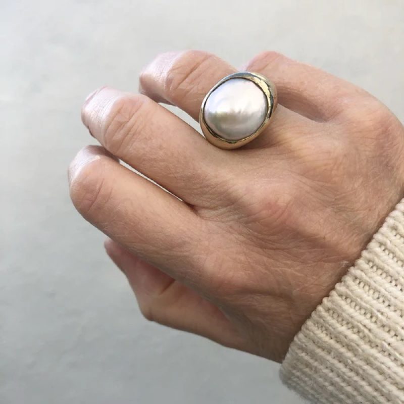 A pearl and gold ring on a hand