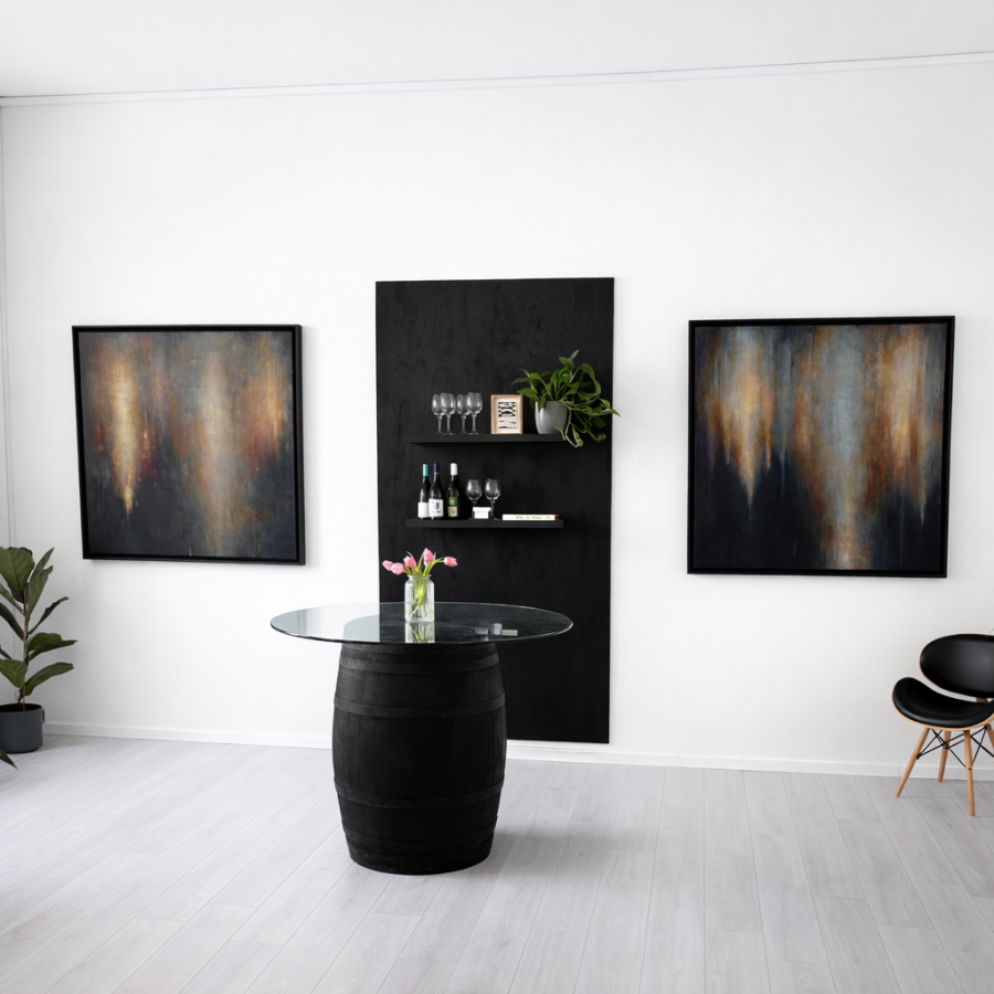A minimalist gallery space with two large, atmospheric abstract paintings on a white wall. A central black tasting table with wine glasses creates a calm, curated exhibition setting.