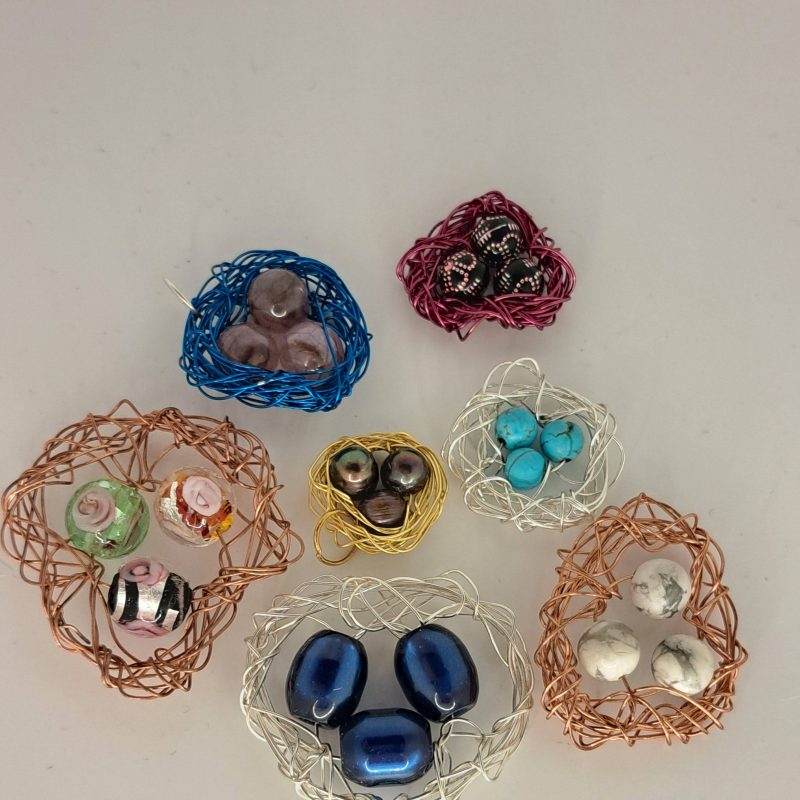Several wire nests hold various beads, including glass, pearl, turquoise, and marble stones. The nests are made of different colored wires such as blue, copper, gold, and silver.