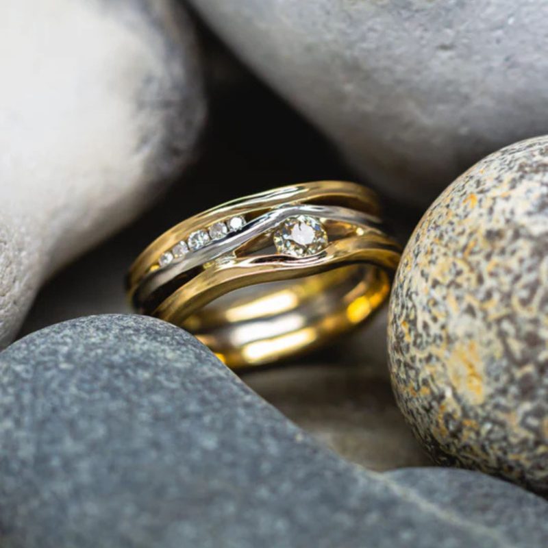 A ring made from three square wires that have been hammered on the side to make them undulating. Diamonds of various sizes are set between the bands. the outer two are yellow gold and the inner one is white gold.