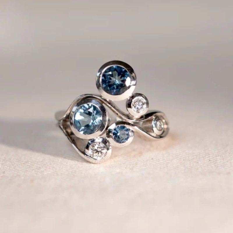 A swirly while gold ring set with diamonds and different shades of blue sapphire