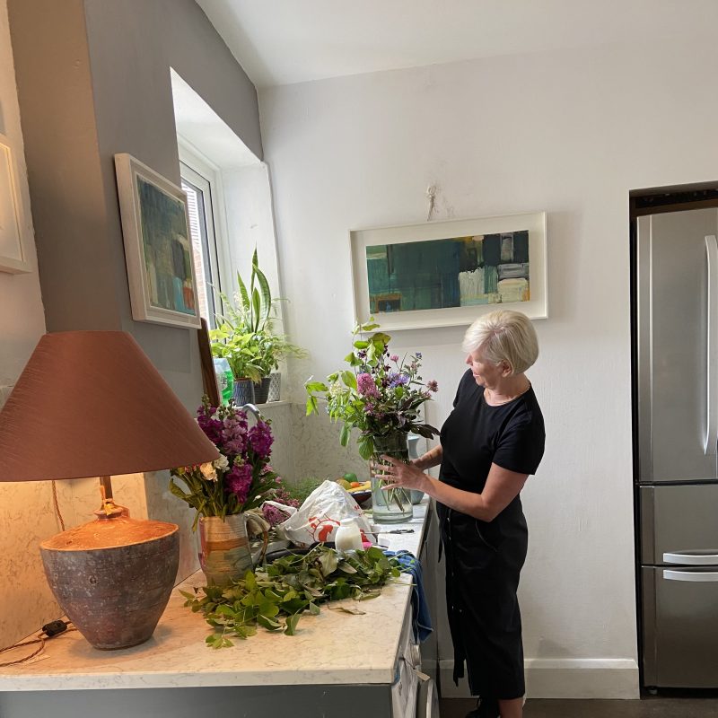 A woman stands at a kitchen counter smiling and arranging flowers