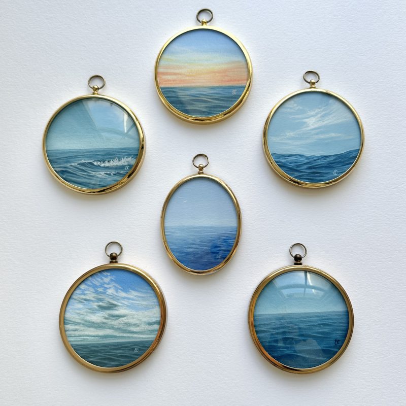 A collection of miniature framed prints hanging from blue ribbons