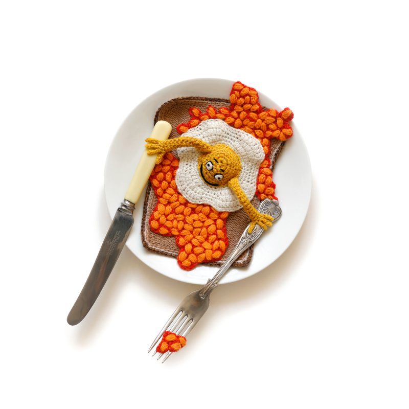 A crocheted egg and embroided baked beans on toast with a plate, knife and fork 
