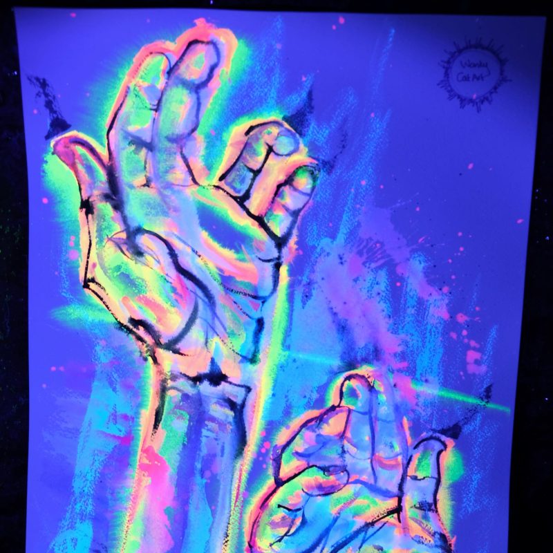 A watercolour painting of two hands illuminated under blacklight, rendered in vibrant neon colors against a deep blue background. The hands are drawn with bold black lines and filled with a swirling, abstract blend of pink, yellow, green, and blue hues.