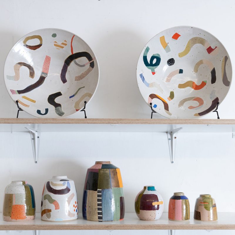 Three shelves containting colourful mags, vases and bowls.