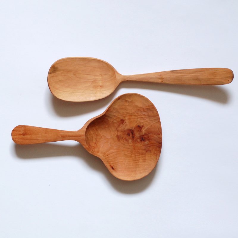 Two Hawthorn Servers hand carved on a white background. one has an oval scoop and the other has a bell shaped scoop.