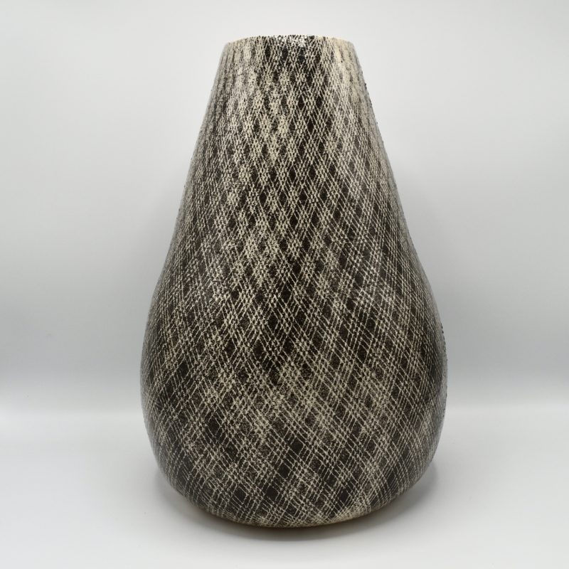 This large vase is more rounded at the bottom and narrows at the top. It is decorated with black slip in a diagonal criss cross pattern made by painting underglaze through a body stocking and leaving the natural light clay colour where it was covered. it is finished in a clear gloss.