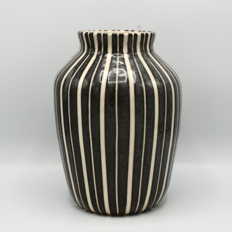 This is a classical shaped vase that is narrow at the bottom and widens towards the top before narrowing at the neck. It is decorated with alternate wide and narrow white stripes on black.
