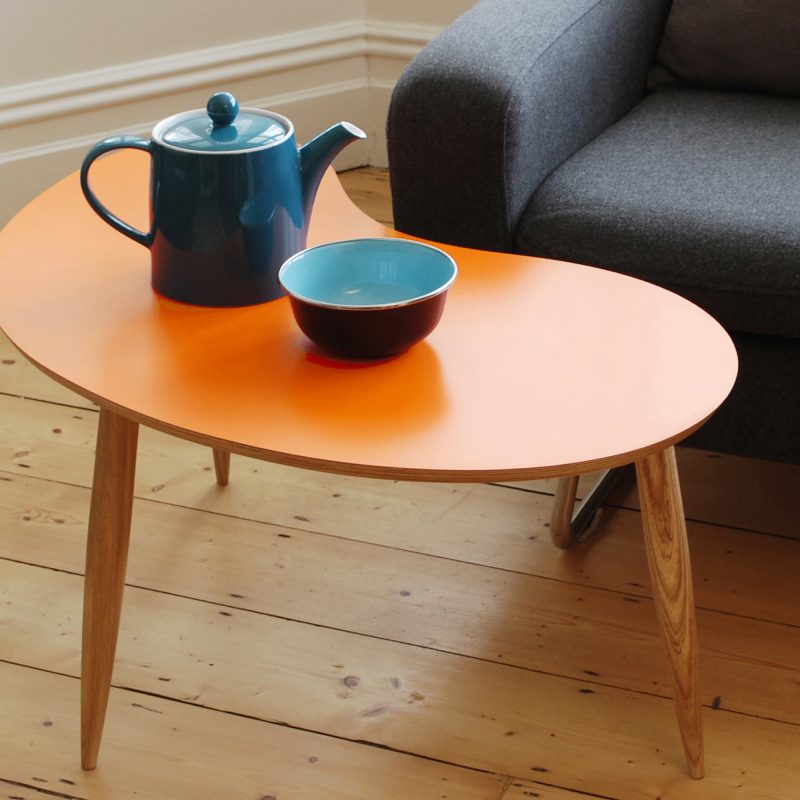 Curved coffee table with an orange top and tapered wood legs