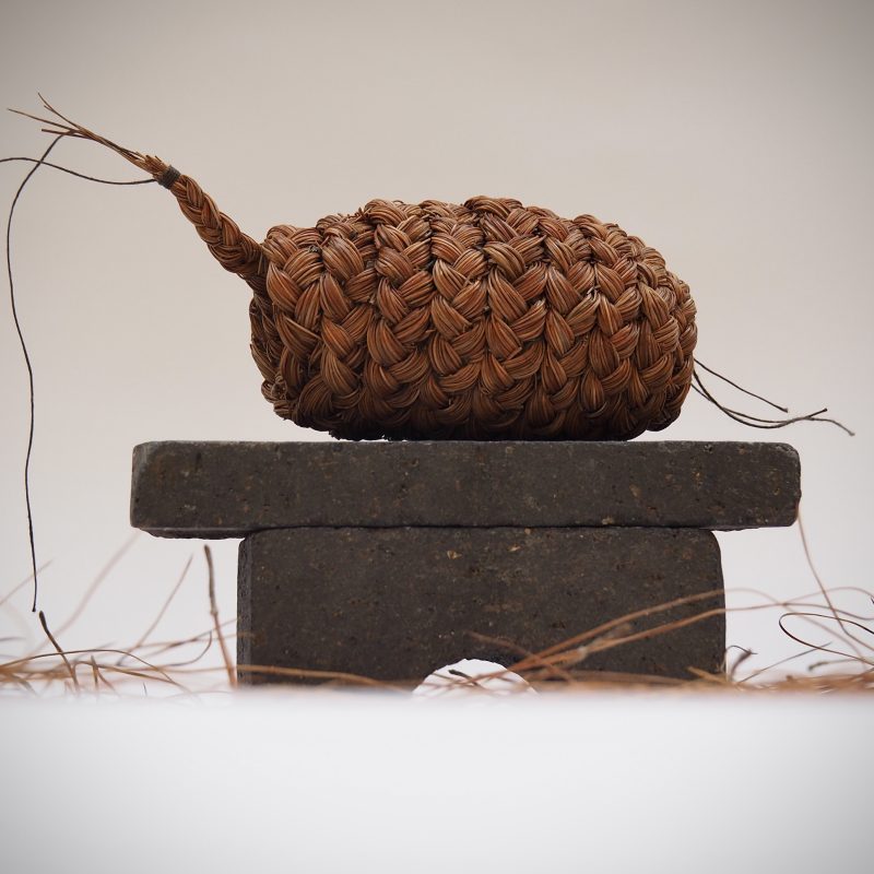 A small cocoon shaped sculpture, made from plaited soft pine needles