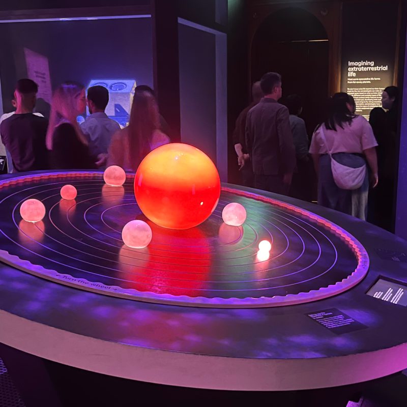 Bright shiny model planets sit on top of a dark circular table within a dark and atmospheric room in the Natural History Museum.