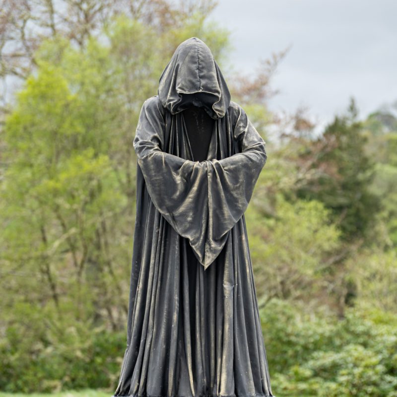 A giant cloaked chess piece stands on a black and white chess board. The figure is cloaked and appears to be made from stone.